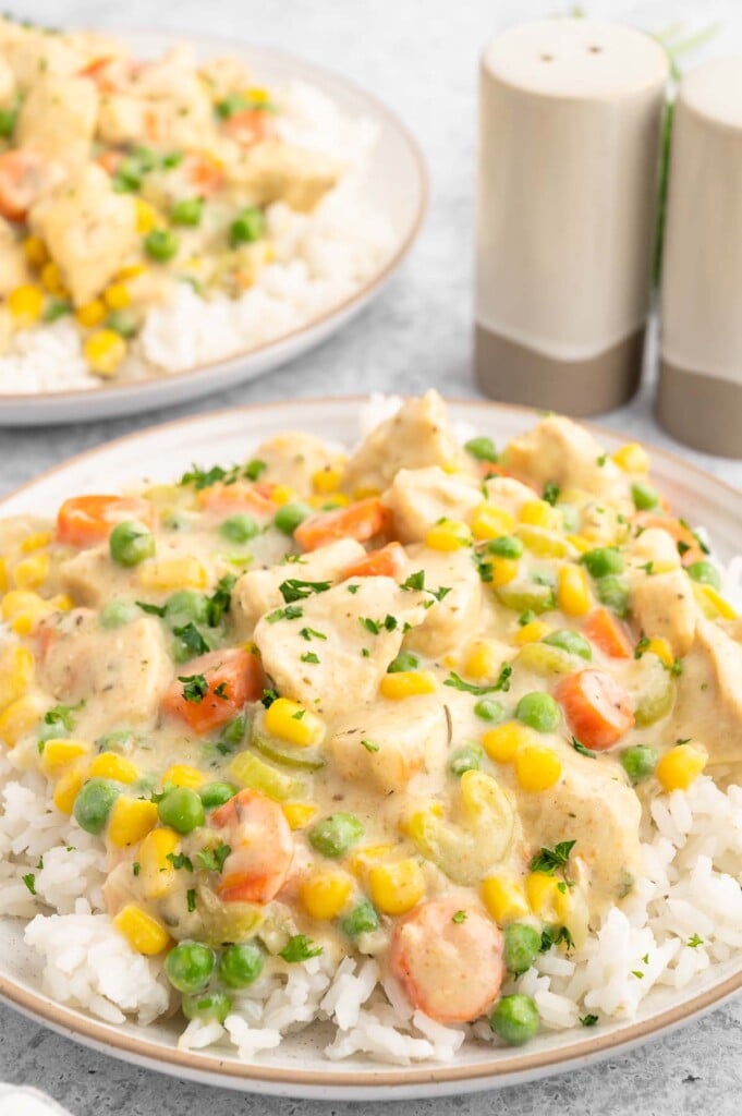 Crustless chicken pot pie filling on a bed of white rice on a plate with another plate in the background.