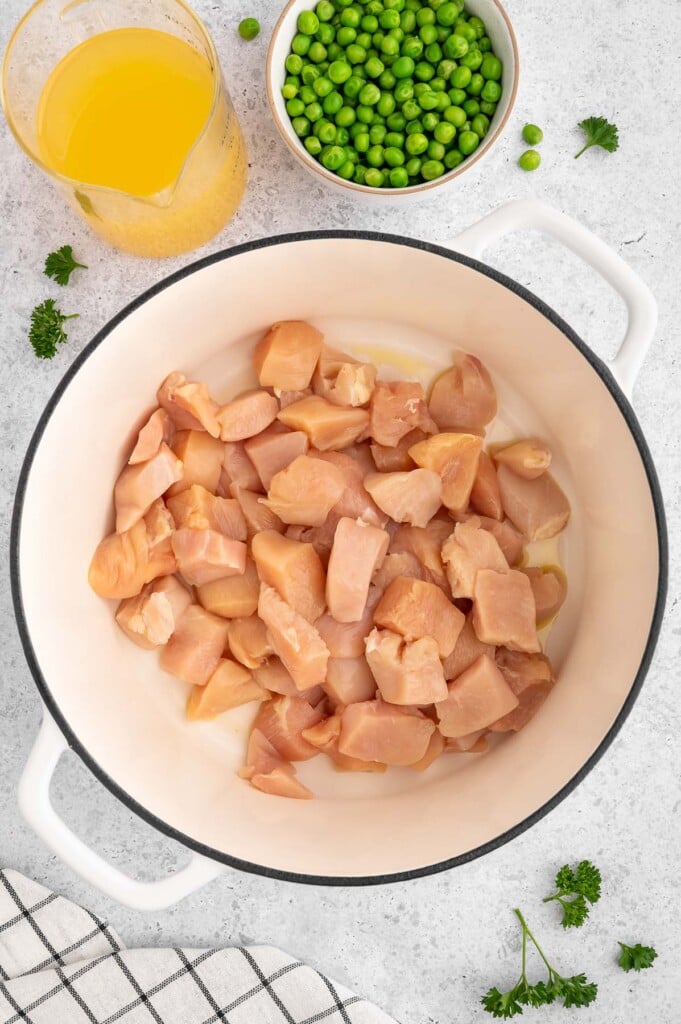 Raw pieces of chicken in a dutch oven with more ingredients for crustless chicken pot pie on the side.