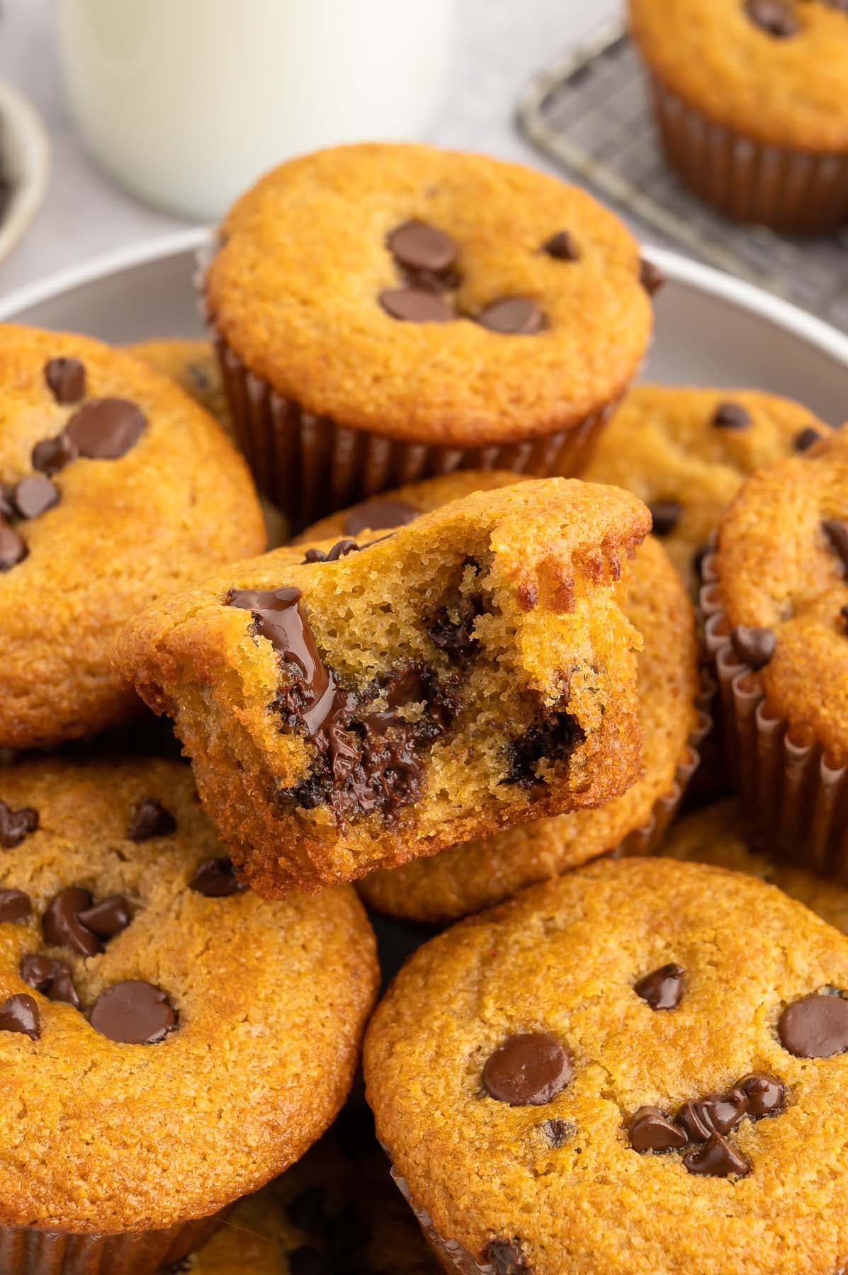 Healthy chocolate chip muffins piled on a grey plate with the muffin in the middle having a bite taken out of it.