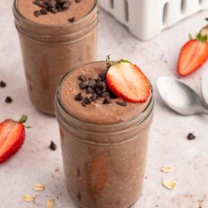 Two mason jars with chocolate overnight oats topped with mini chocolate chips and sliced strawberries.