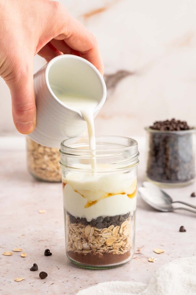 Milk being poured into a mason jar filled with cocoa powder, oats and mini chocolate chips.