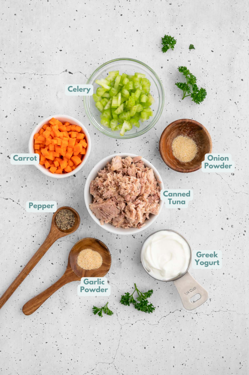 Ingredients for tuna salad without mayo in small white bowls on a grey background: yogurt, tuna, veggies and spices