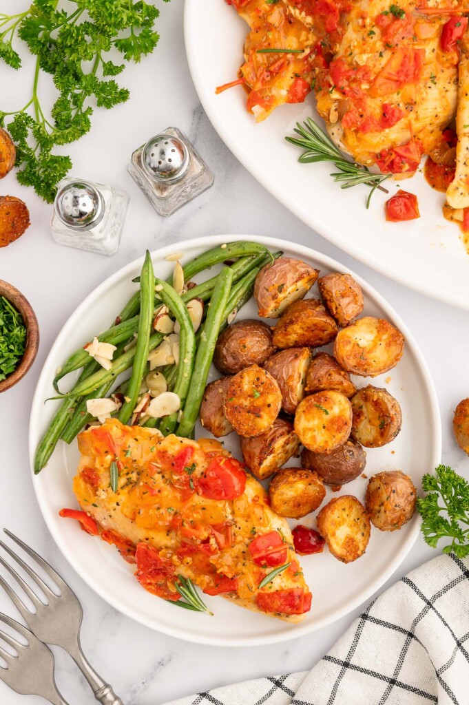 Braised chicken Scarpariello on a white plate with garlic potatoes and green bean almondine on the side.