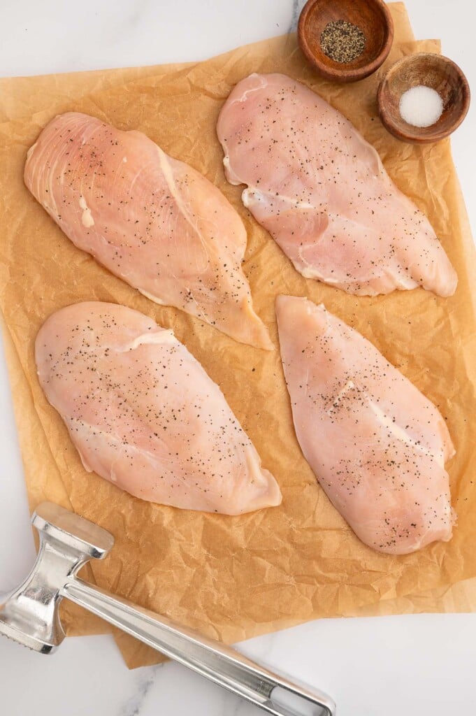 Four butterflied Chicken Breasts on a piece of parchment paper seasoned with salt and pepper.