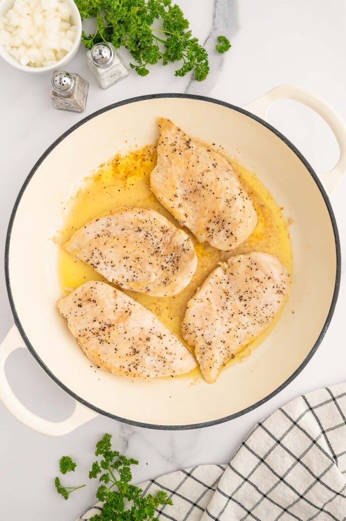Four chicken breasts cooking in olive oil in a dutch oven.