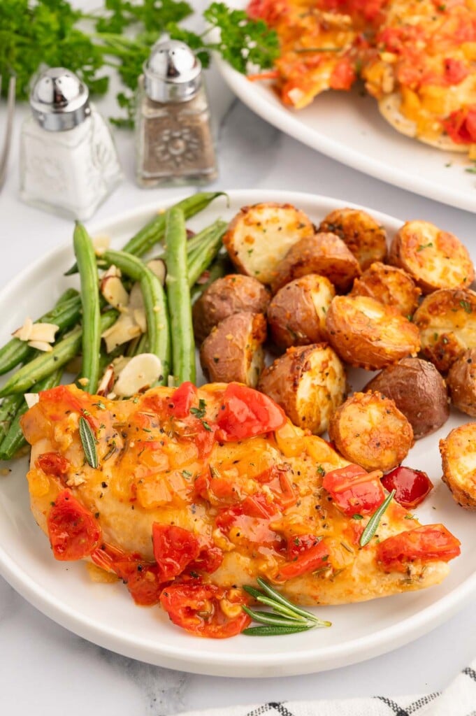 Braised chicken Scarpariello on a white plate with garlic potatoes and green bean almondine on the side.