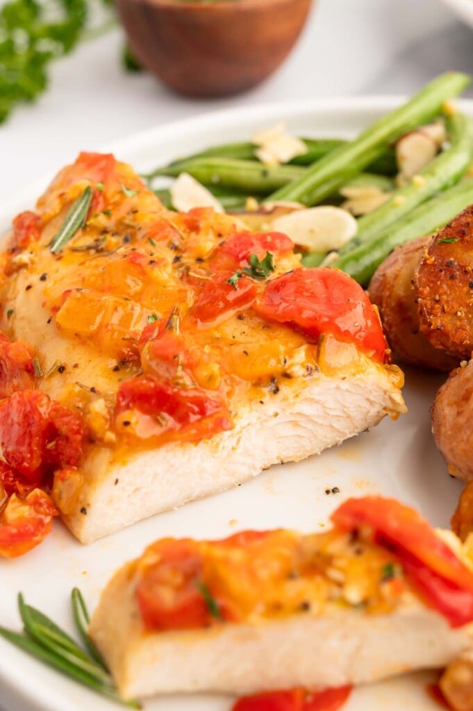 Chicken Scarpariello cut in half on a white plate with green beans and potatoes on the side.