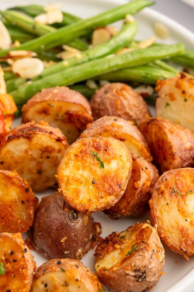Roasted Garlic Parmesan Potatoes on a white plate with green beans in the background.