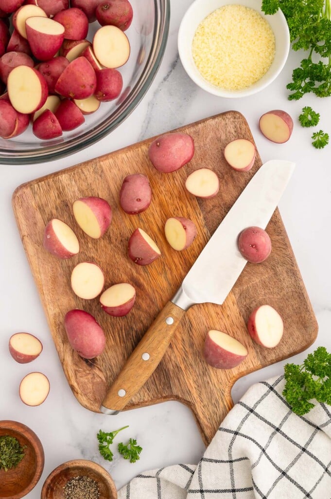 Halved red baby potatoes on a cutting board with a knife.