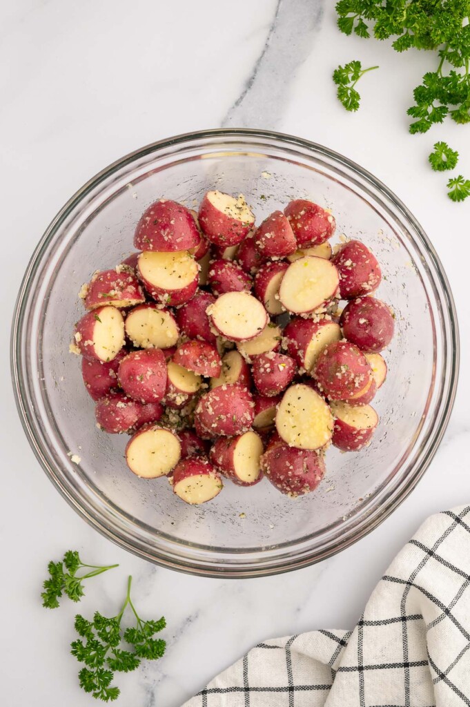 Halved red potatoes in a clear bowl tossed with olive oil and spices.