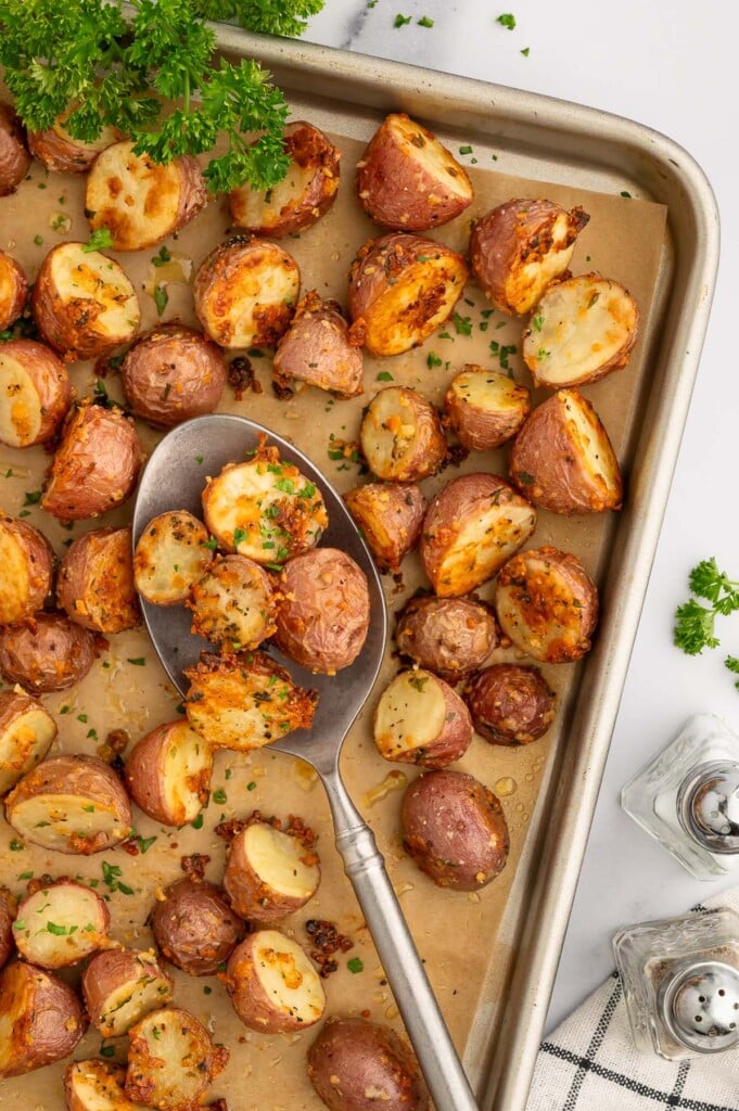 Garlic Roasted Potatoes on a parchment lined baking sheet with a spoon scooping up some potatoes.