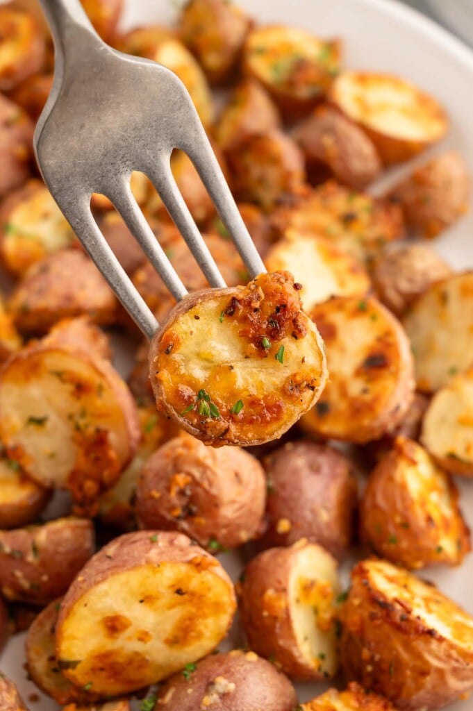 A fork taking a garlic roasted potato off a platter with the potatoes.