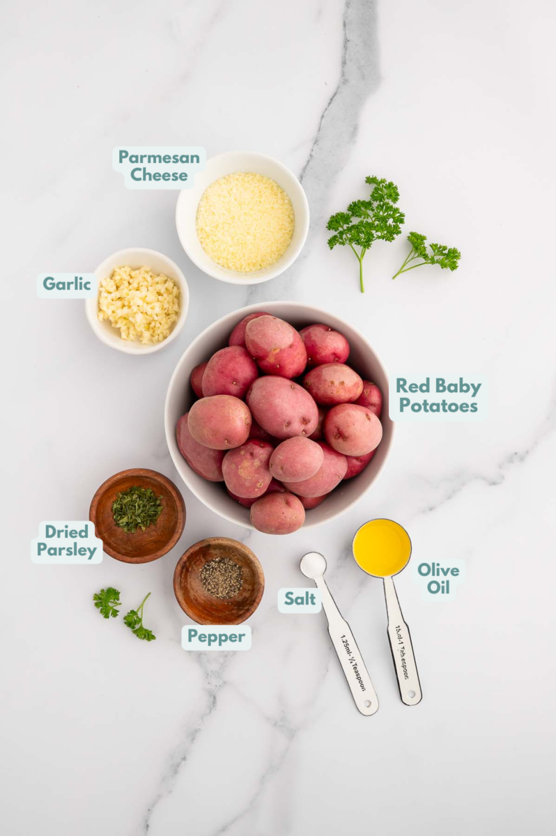 Ingredients for crispy garlic roasted potatoes in small bowls: red baby potatoes, olive oil, dried parsley, salt, pepper, parmesan cheese, garlic