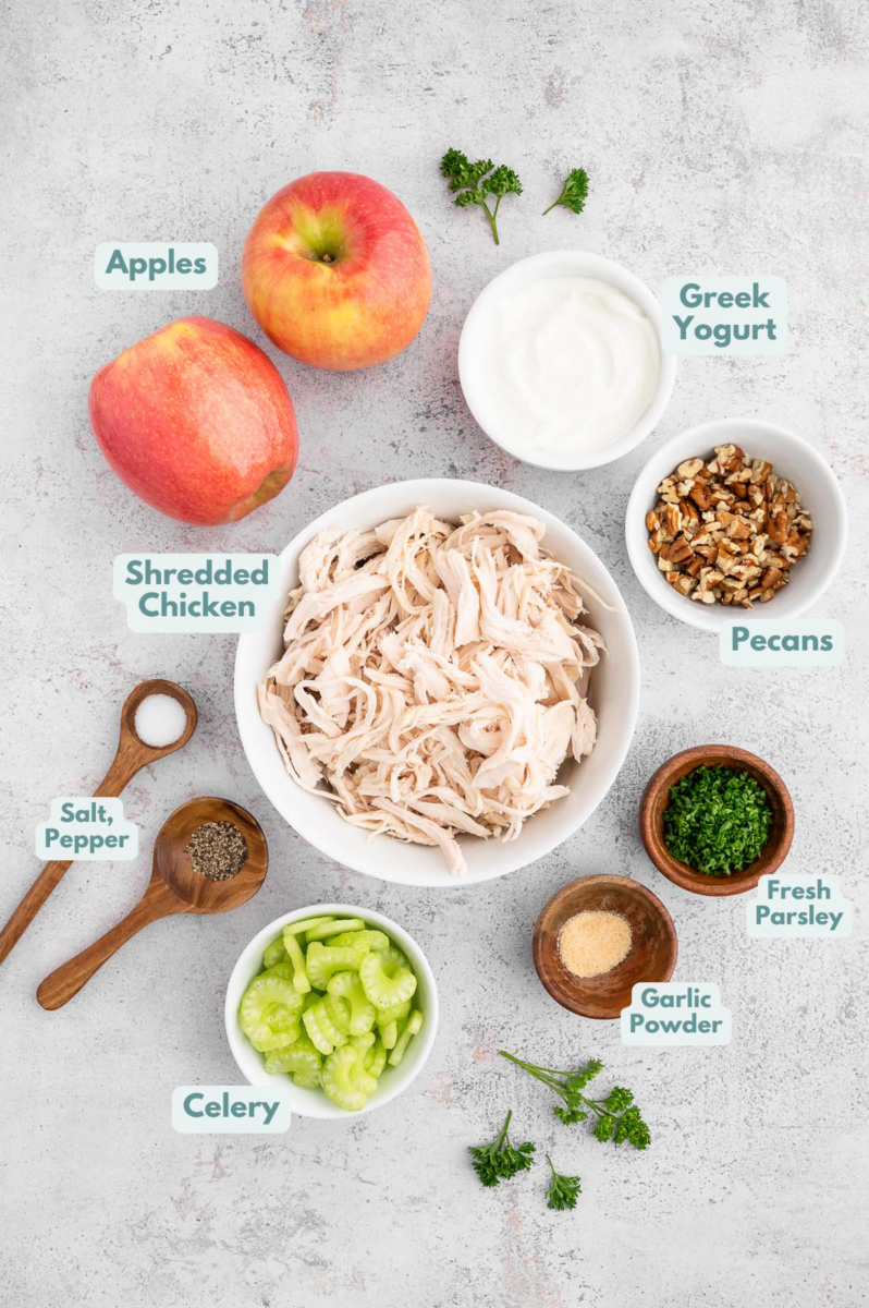 Ingredients for Greek Yogurt Chicken salad laid out on a grey background in small white bowls.