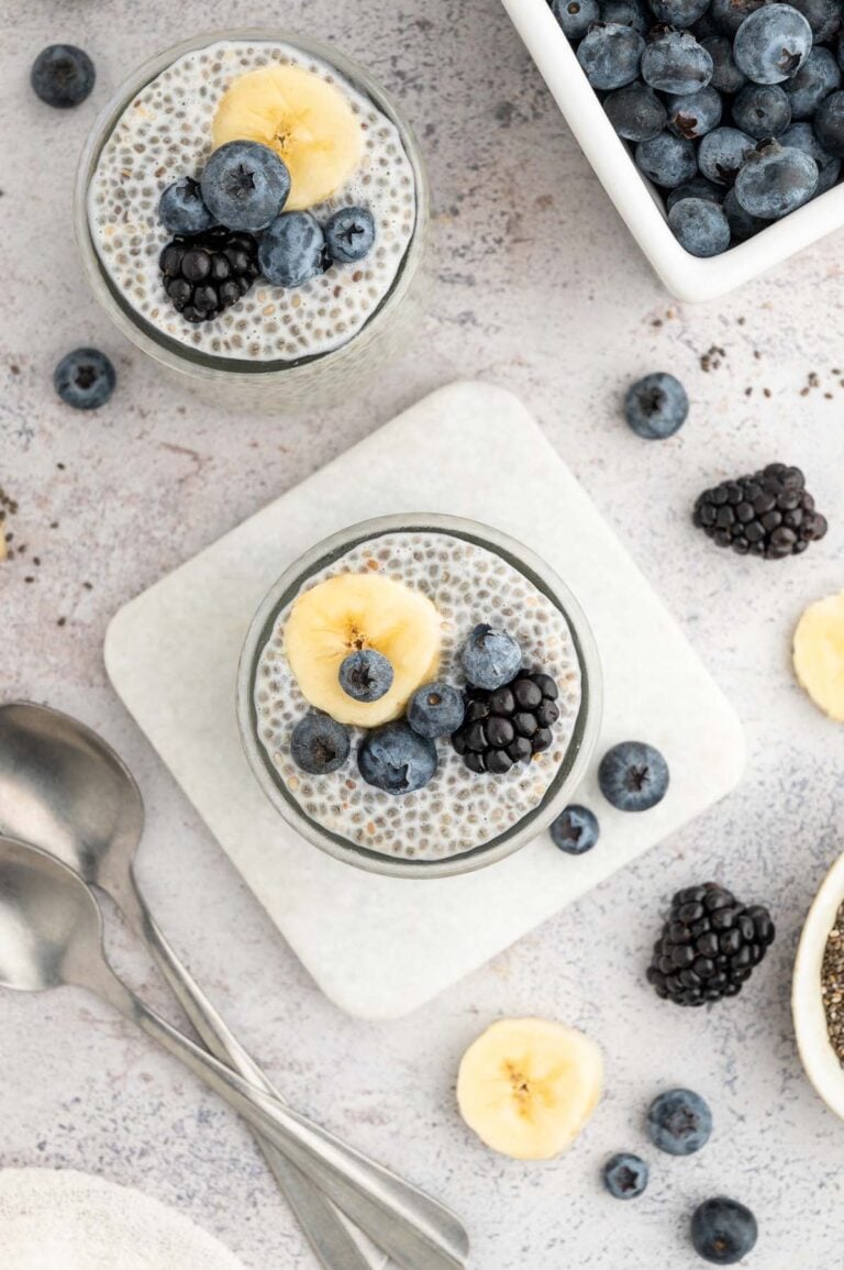An overhead shot of two jars of chia seed pudding topped with berries and banana slices.