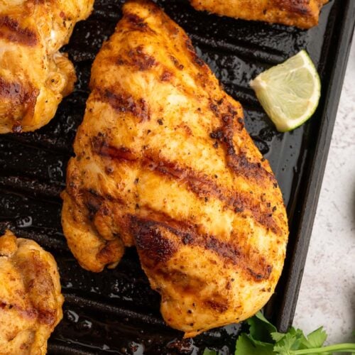 Chili Lime Chicken Breasts on a cast iron grill with a lime slice and cilantro on the side.