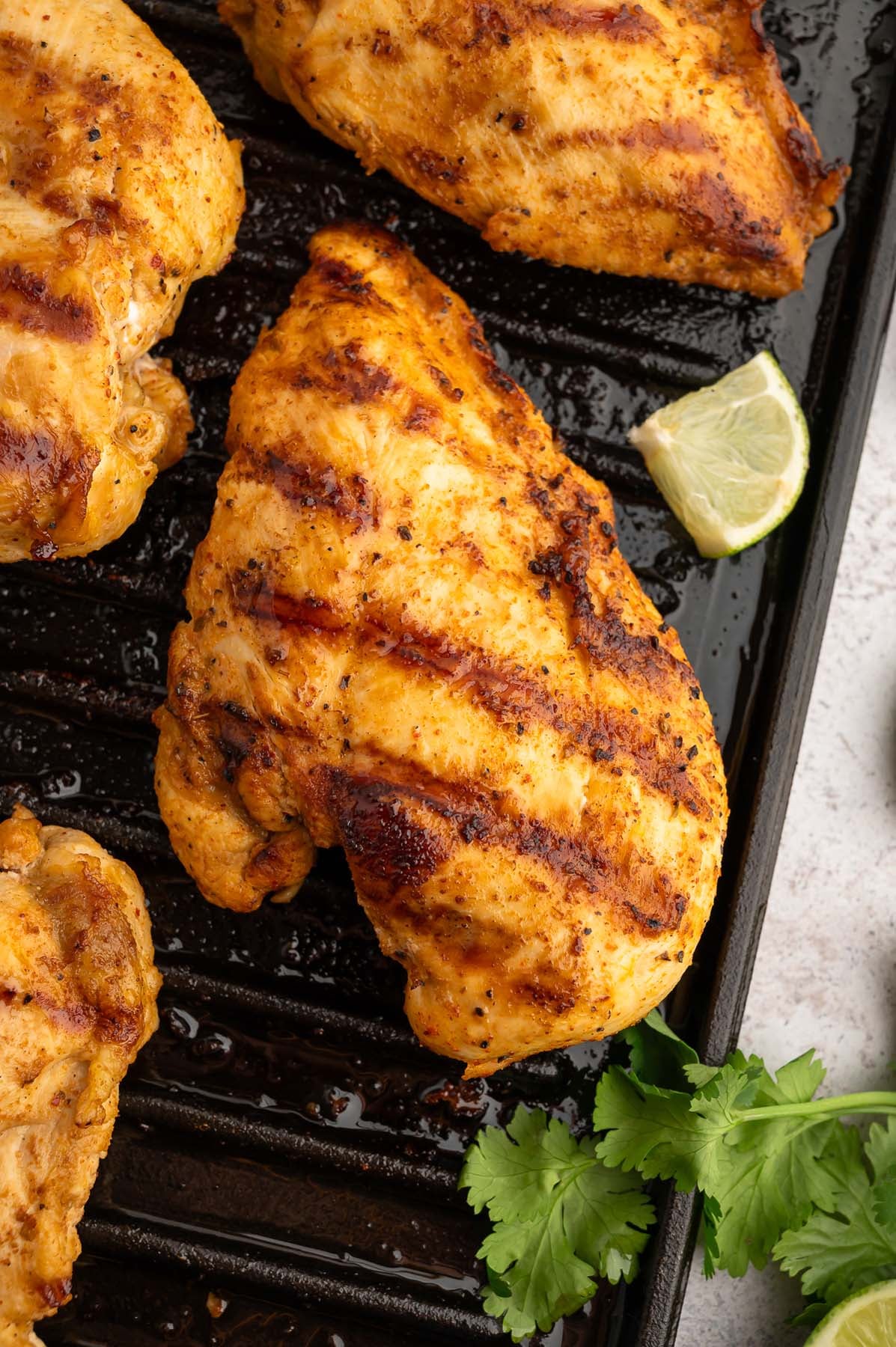 Chili Lime Chicken Breasts on a cast iron grill pan with a lime slice and cilantro on the side.
