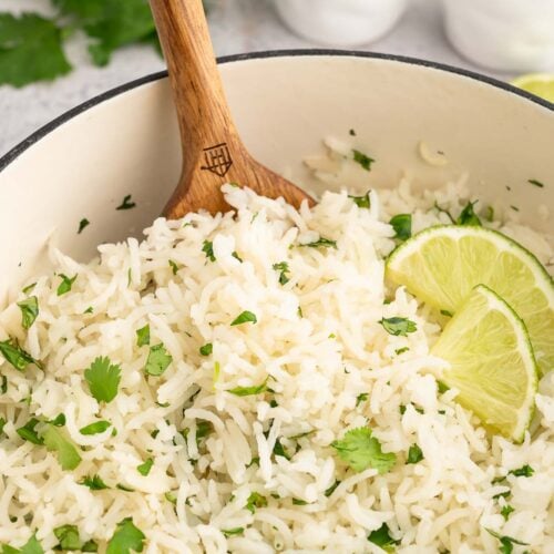 Cilantro lime rice in a pot garnished with chopped cilantro and lime wedges with a spoon in it.
