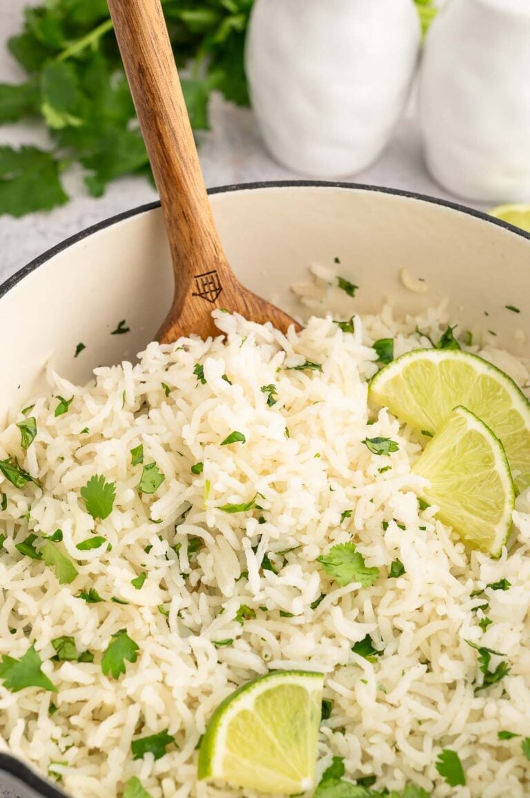 Cilantro lime rice in a pot garnished with chopped cilantro and lime wedges with a spoon in it.