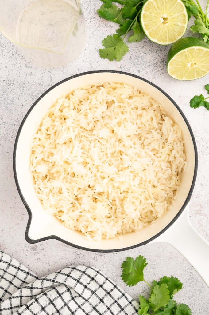 Cooked white rice in a pot with limes and cilantro on the side.
