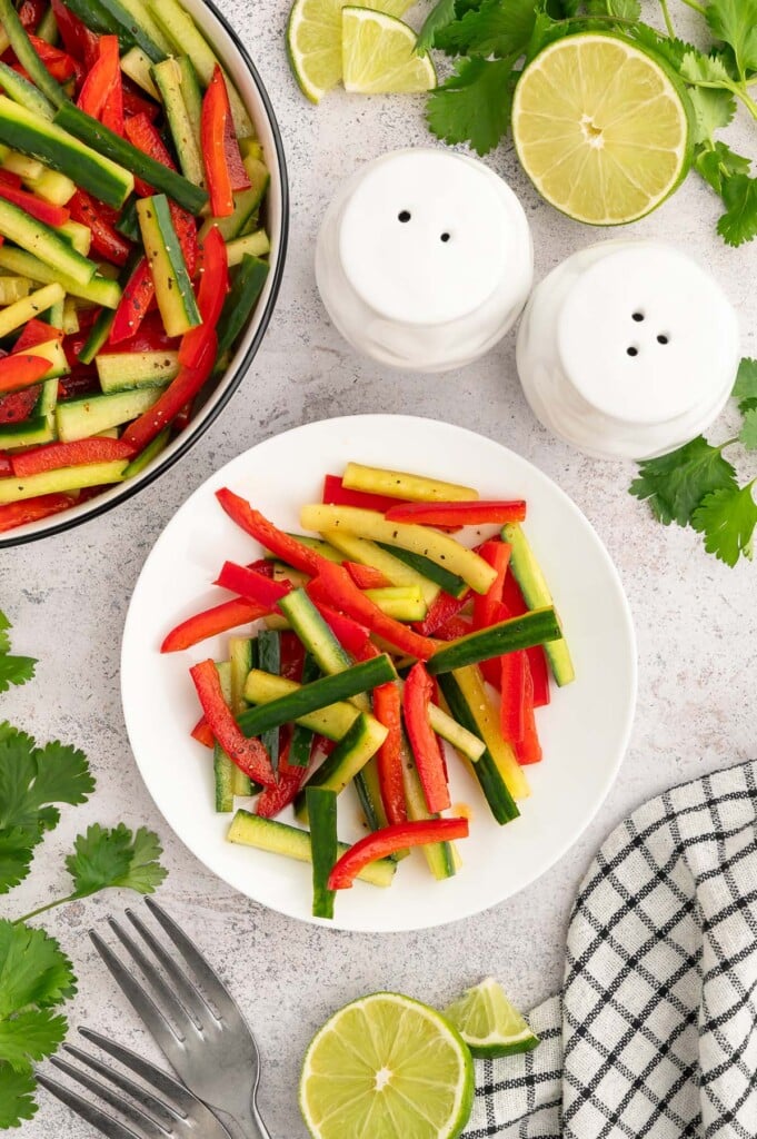 Marinated veggie salad on a white plate with a bowl of the salad on the side. 