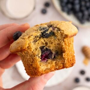 A hand holding up a blueberry protein muffin with a bite taken out of it.