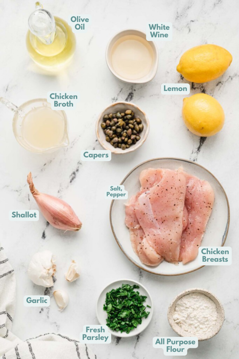 Ingredients for lemon chicken piccata in small bowls on a white background: chicken breasts, salt, pepper, all purpose flour, olive oil, shallot, garlic, white wine, chicken broth, capers, lemon