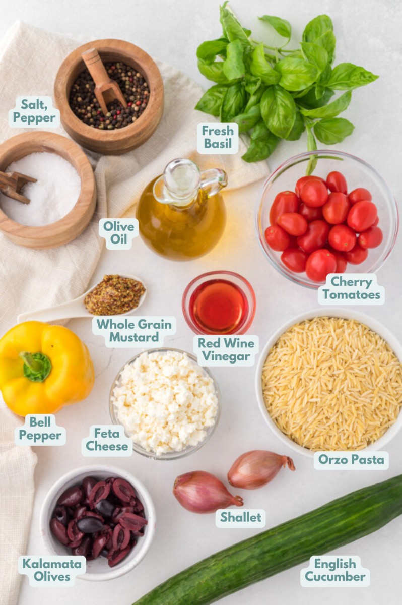 Ingredients for orzo salad in white bowls: orzo pasta, english cucumber, cherry tomatoes, bell pepper, feta cheese, shallots, kalamata olives, fresh basil, olive oil, red wine vinegar, whole grain mustard, pepper