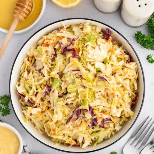 Vinegar based coleslaw in a large bowl with more ingredients on the side.