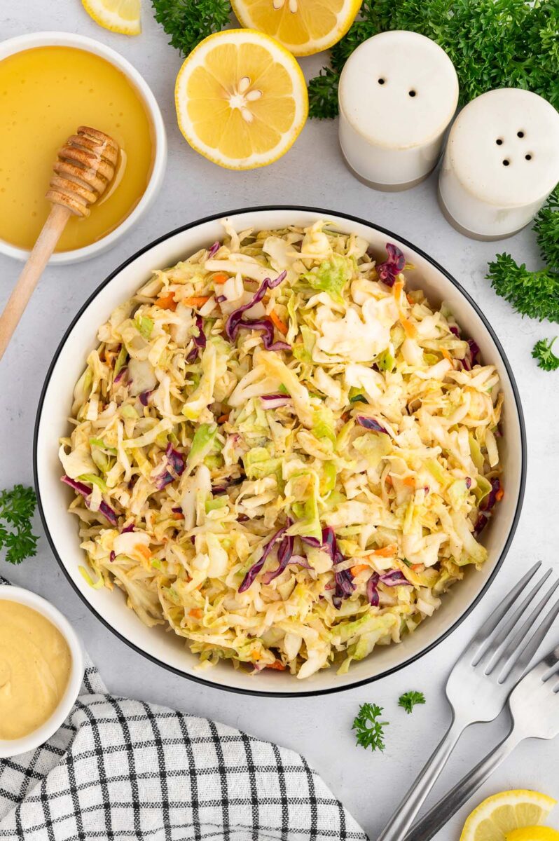 Vinegar based coleslaw in a large bowl with more ingredients on the side.