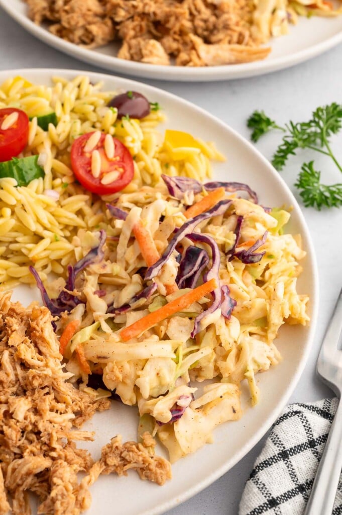 Close up of vinegar based coleslaw on a plate with bbq shredded chicken and orzo salad on the side.