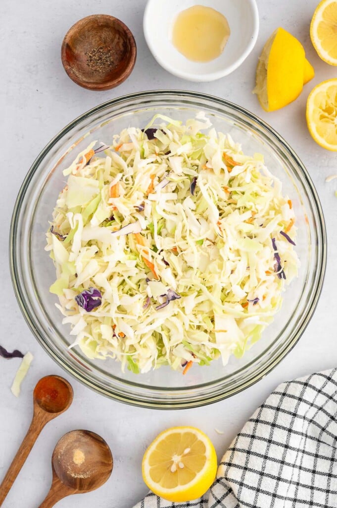 Healthy vinegar coleslaw in a large clear bowl before being mixed together.