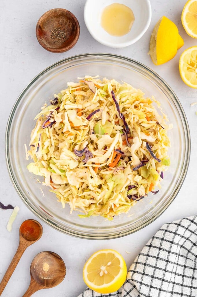 Vinegar based coleslaw in a clear bowl with lemons and empty bowls on the side.