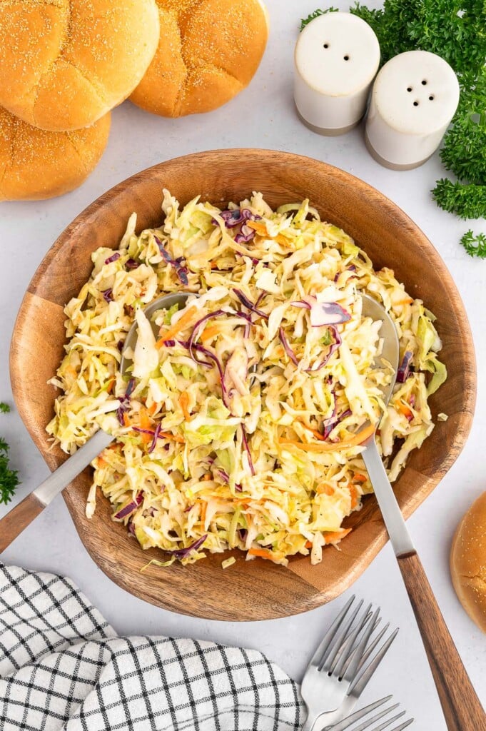 Vinegar coleslaw in a large wooden bowl with large spoons in the bowl. 