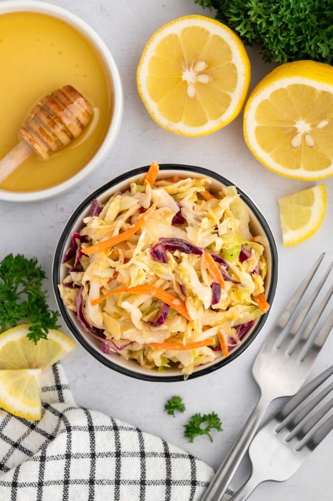 Healthy vinegar coleslaw in a small bowl with sliced lemon and honey on the side.