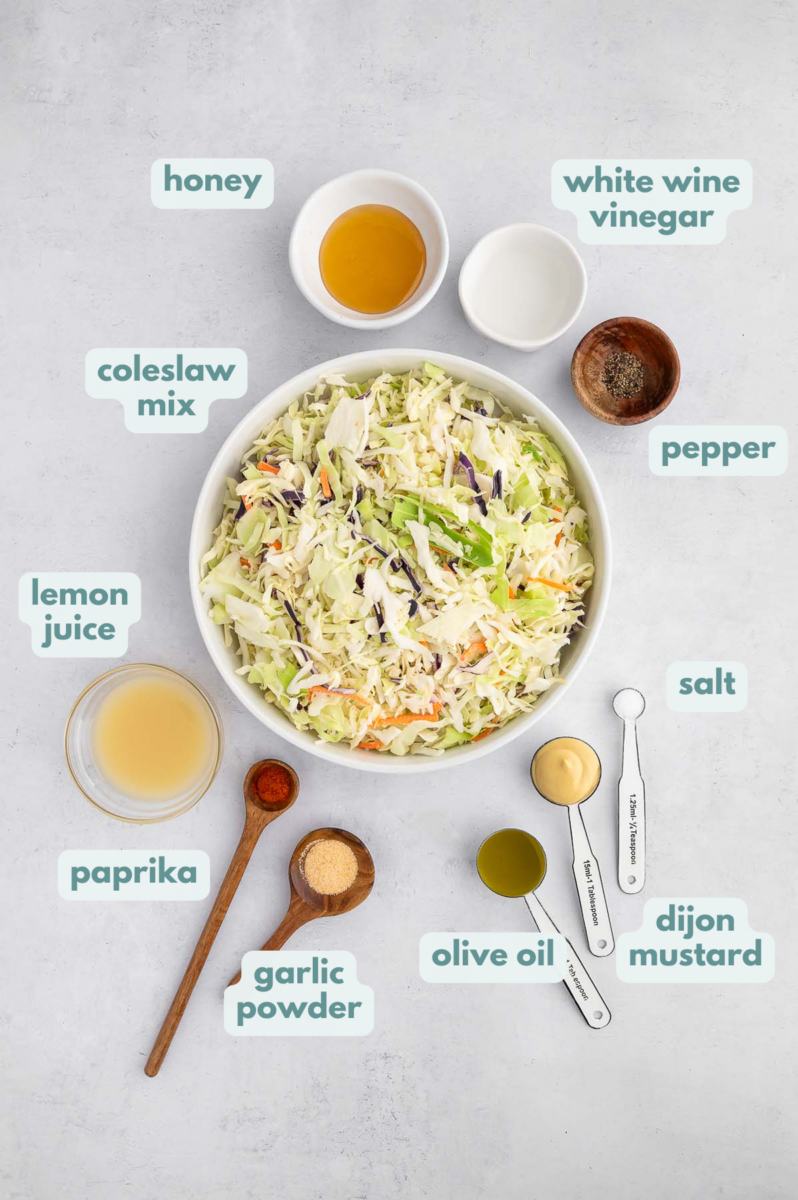 Ingredients for vinegar coleslaw in small bowls: honey, lemon juice, white wine vinegar, extra virgin olive oil, dijon mustard, salt, pepper, garlic powder, paprika, coleslaw mix
