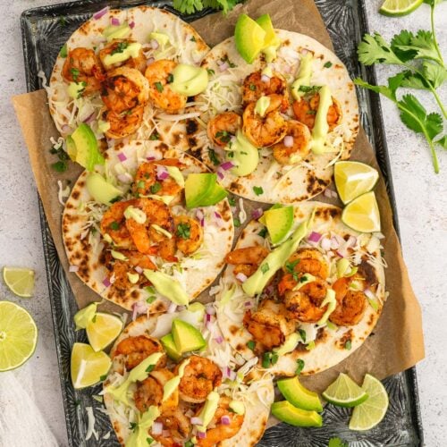 5 Chili Lime Shrimp Tacos on a black sheet pan with chili powder, limes, and cilantro on the side.