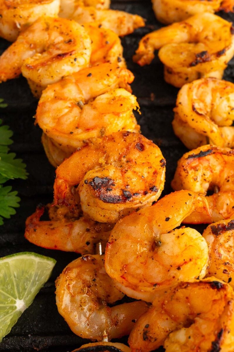 Close up of chili lime shrimp skewers on a black grill with a lime on the side.