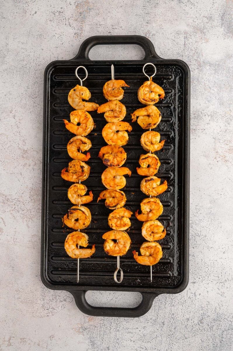 3 Chili Lime Shrimp Skewers on a black stove top grill.
