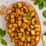 Homemade croutons piled on a platter with fresh basil leaves around it.