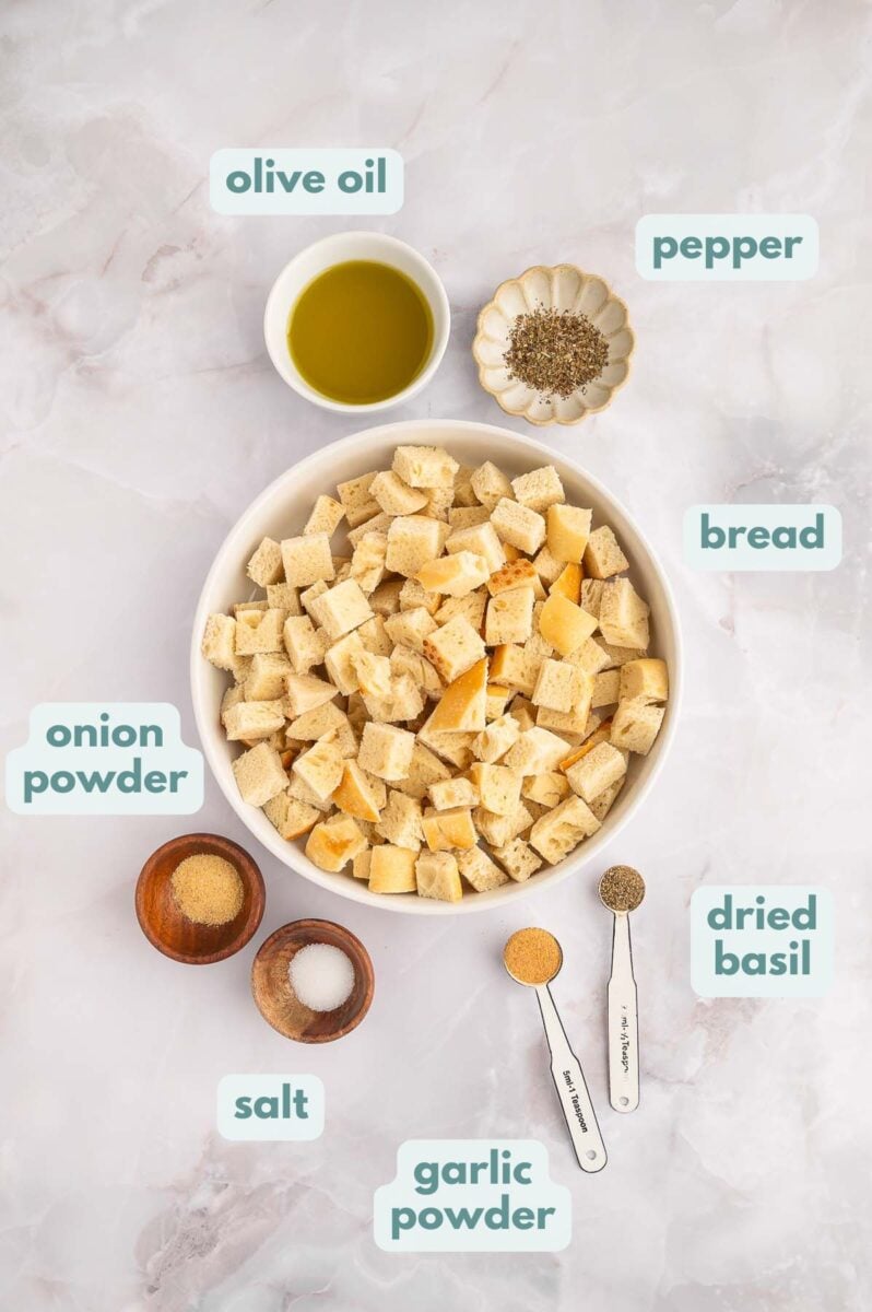 Ingredients for Homemade croutons in small bowls and labeled: olive oil, pepper, bread, dried basil, garlic powder, salt, onion powder