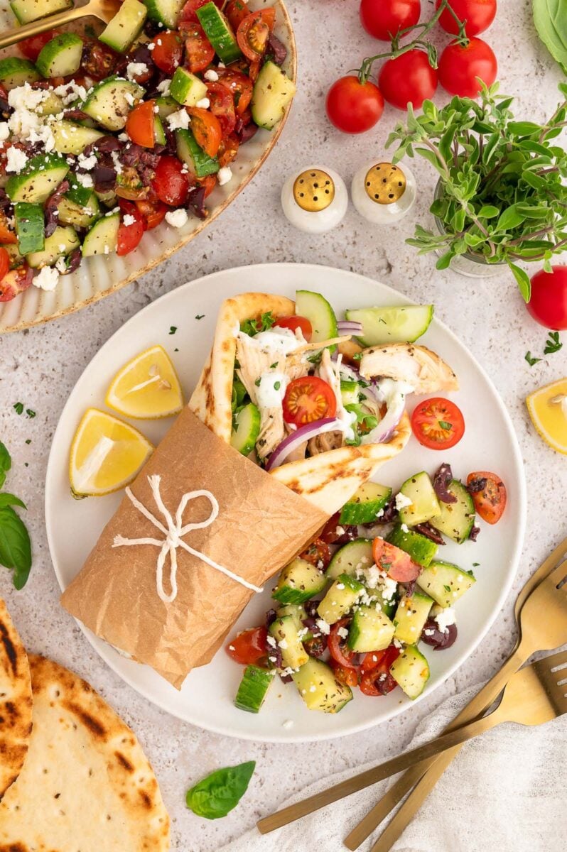 An overhead shot of a greek shredded chicken pita with a chopped greek salad on the side.