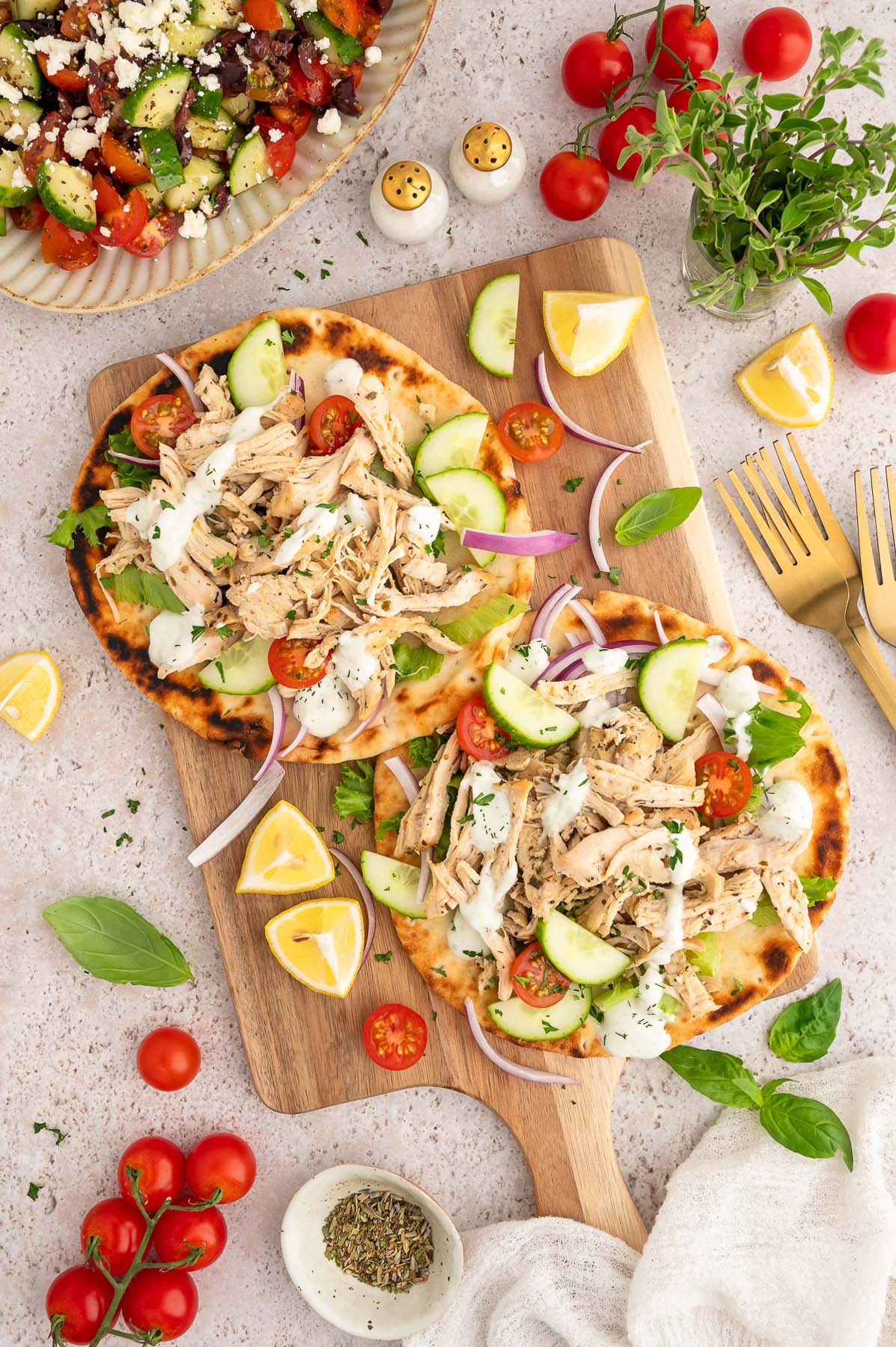 An overhead shot of two open-faced pitas topped with braised and pulled chicken, cherry tomatoes, sliced cucumbers, and red onions.