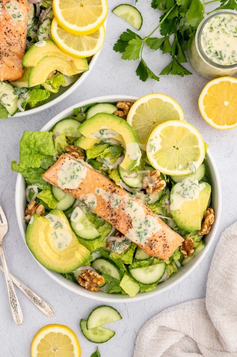 An overhead shot of a salmon salad topped with healthy tahini dressing and a jar of dressing on the side.