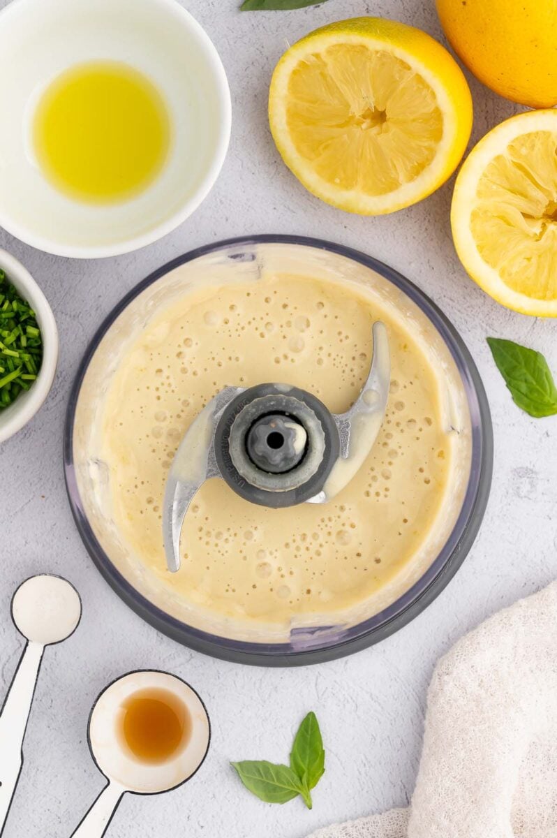 Tahini Dressing blended in a food processor before adding fresh herbs with lemons on the side.