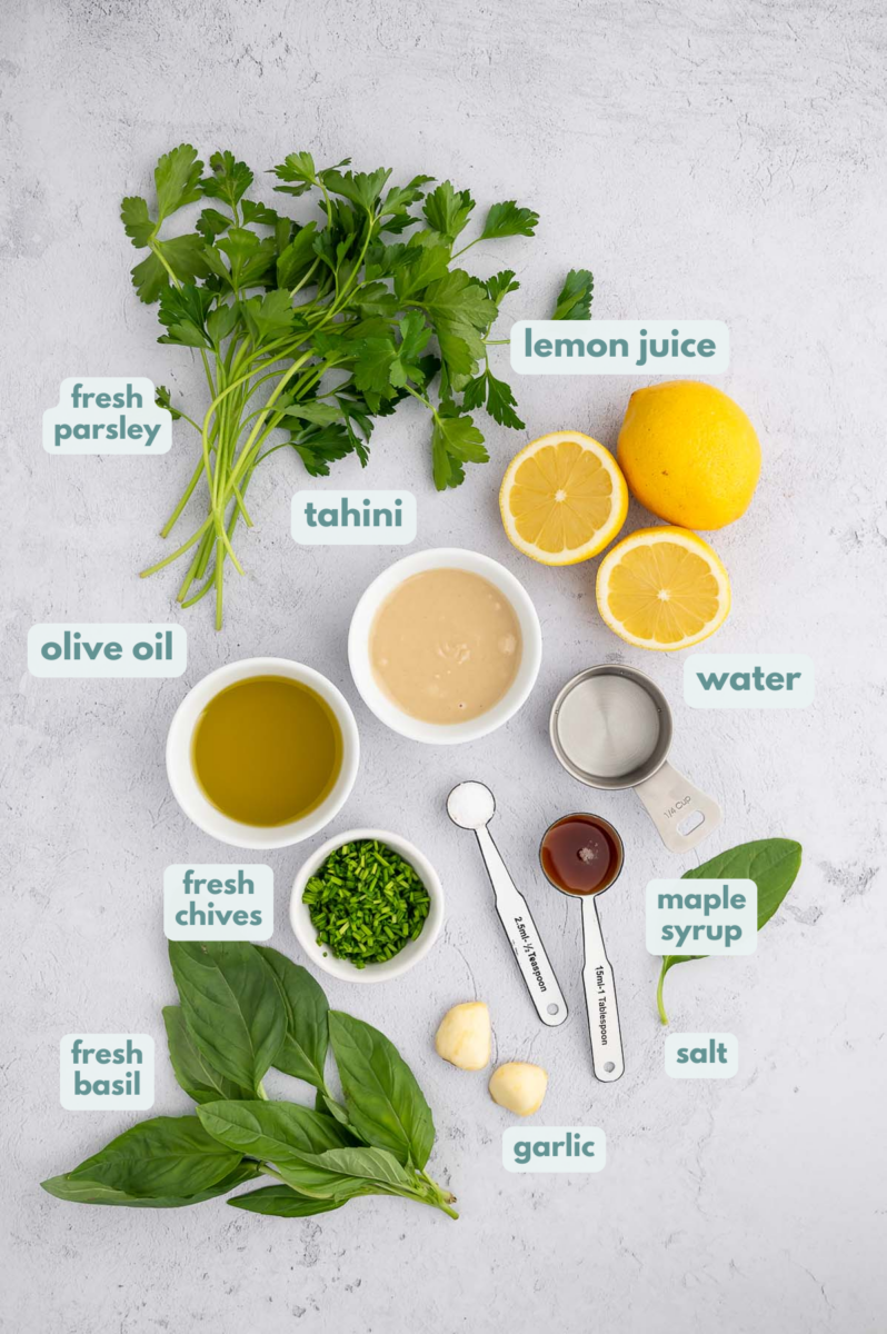 Ingredients for tahini lemon dressing in small bowls: lemon juice, raw tahini, olive oil, maple syrup, garlic, salt, fresh basil, parsley and chives.