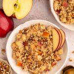 Apple Oatmeal in a shallow white bowl with sliced apples garnishing and another bowl on the side.