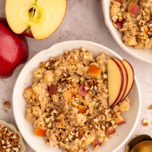 Apple Oatmeal in a shallow white bowl with sliced apples garnishing and another bowl on the side.