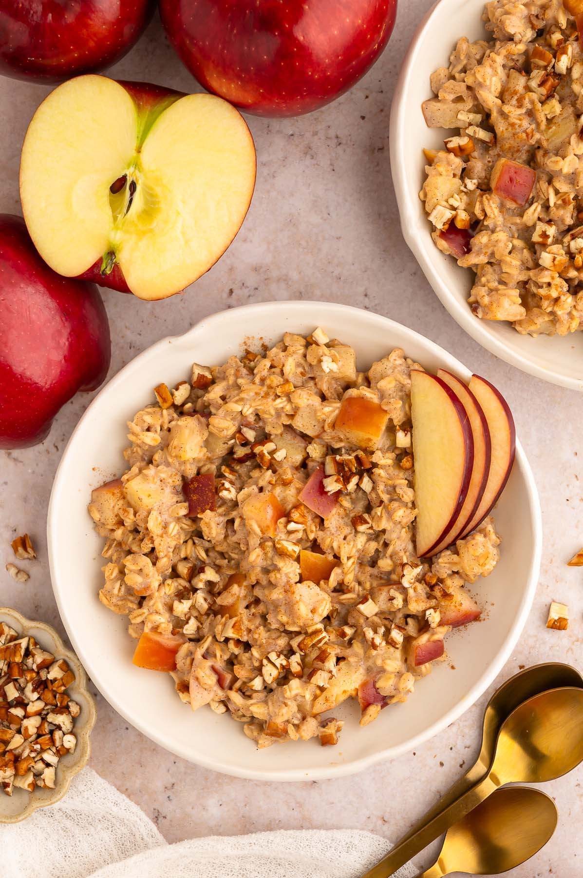 Apple oatmeal in a shallow white bowl with sliced apples for garnish, and another bowl on the side.
