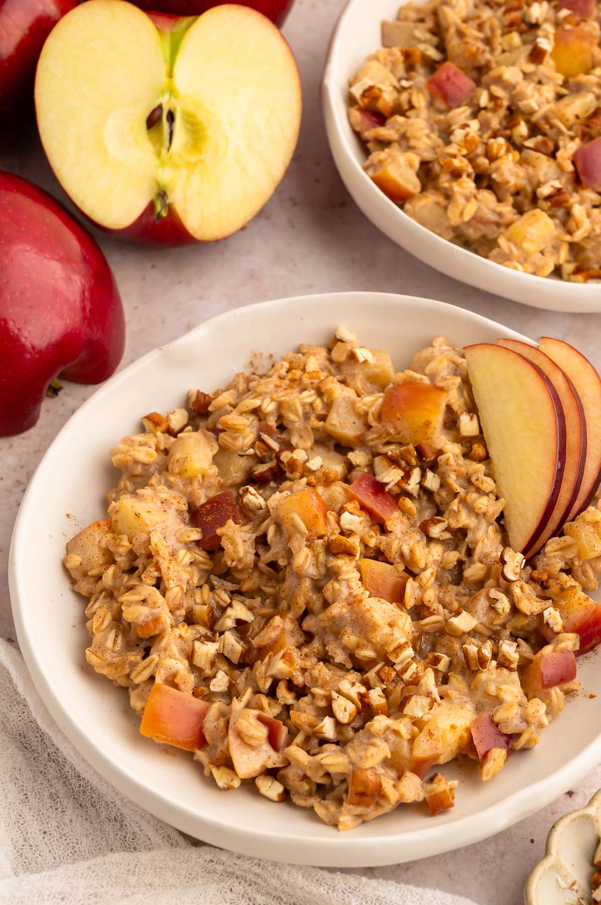 A close up of apple oatmeal in a shallow white bowl with another bowl of the warm cereal off to the side.